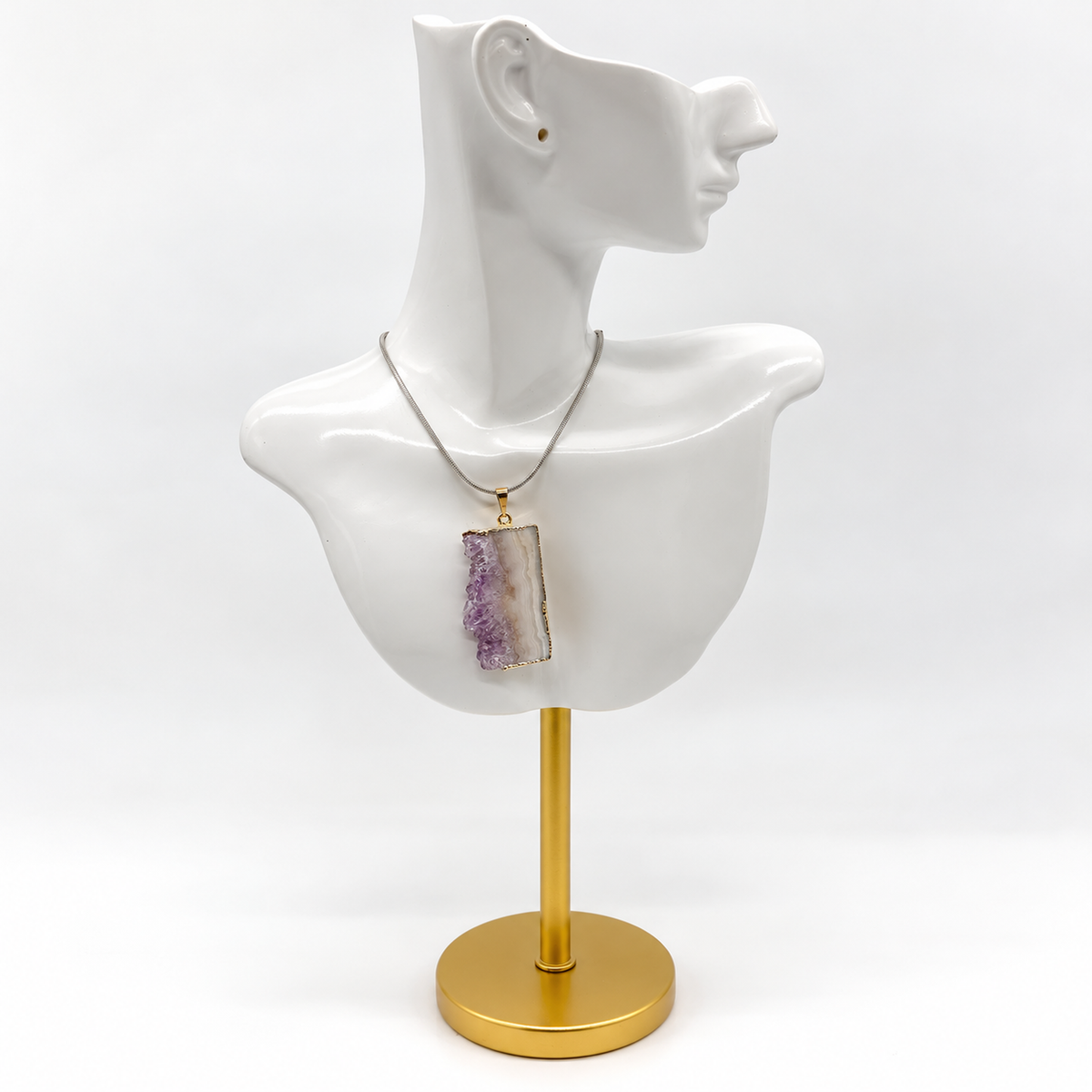 Amethyst druzy pendant necklace displayed on glossy white sculptural jewelry bust with gold stand and circular base